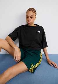 Juoda medvilnės marškinėliai su apvalia iškirpte ir maža logo, derinami su žaliais šortais, turinčiais tris geltonas juosteles ir "adidas" emblemą.