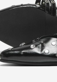 Zapato negro de punta afilada hecho de material brillante con acentos de tachuelas plateadas. Presenta una suela de goma negra texturizada para mayor agarre.