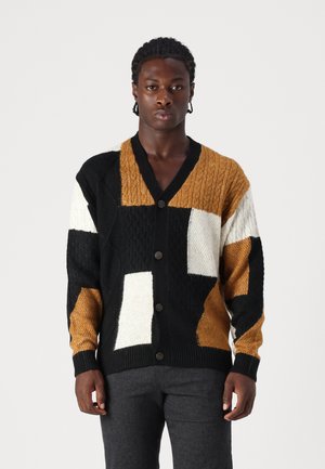 Cárdigan de punto con diseño de patchwork en negro, blanco y mostaza, con patrones texturizados y cinco cierres de botones.