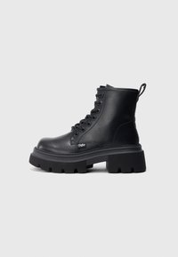 Botines negros de tobillo hechos de cuero suave, con una suela de goma gruesa, puntera redonda, diseño de cordones, y un lazo en el talón para facilitar el uso.