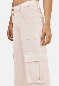 Pantalones cargo de color rosa claro con un corte relajado, bolsillos laterales y dos botones decorativos en la cintura. Tejido de algodón con una textura suave.