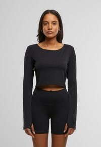 Must must sleeves crop top mustest kangas, millel on ümar kaelus ja istuv disain, koos kõrge vöökoht mustade lühikesed püksid.