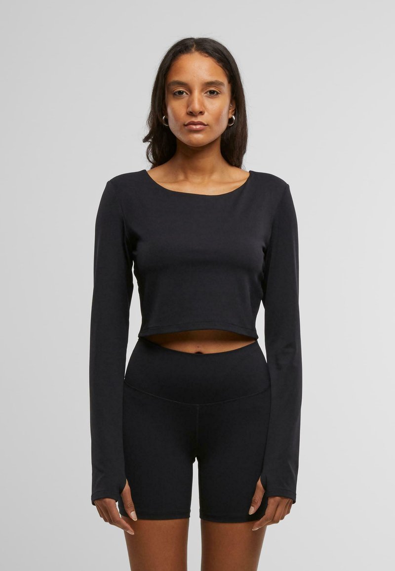 Must must sleeves crop top mustest kangas, millel on ümar kaelus ja istuv disain, koos kõrge vöökoht mustade lühikesed püksid.