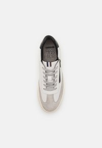 Férfi sneaker, amely szürke bőrből és velúrból készült, kerek orrú, szürke fűzőkkel, fekete részletekkel és logóval a nyelvén.
