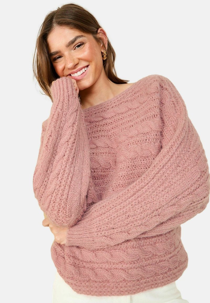 Roza pletena jopica z debelimi kabli in rebrastimi vzorci, z oversize rokavi in širokim izrezom, izdelana iz mehke, teksturirane tkanine.