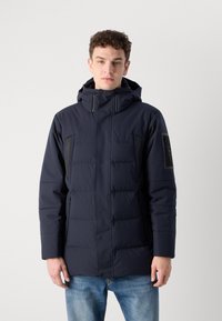Giacca imbottita blu navy con cappuccio, tasche laterali con zip, dettagli a pannello e una texture liscia e leggermente lucida.