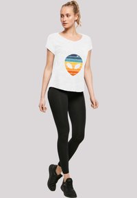 White short-sleeve t-shirt with a colorful alien graphic, paired with black leggings and black sneakers, showcasing a casual athletic style.
