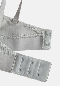 Primo piano delle spalline di un reggiseno grigio chiaro che mostrano i ganci con occhielli con due ganci da un lato e tre file di occhielli dall'altro.