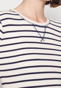 Pruhovaný dlouhý rukáv top s off-white a námořnickými modrými horizontálními pruhy, žebrovanou strukturou a kulatým výstřihem s kontrastním šitím.