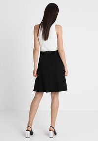 Falda negra acampanada con una textura suave, cintura alta y cierre con cremallera en la parte trasera. Combinada con una blusa sin mangas de punto blanca.