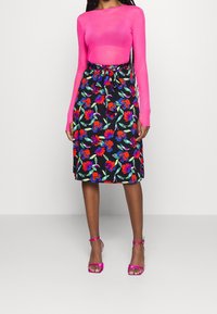 Top rosa a maniche lunghe con un design aderente abbinato a una gonna nera a fiori con motivi rossi e blu, legata in vita.