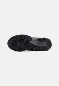 Semelle en caoutchouc noire avec des crampons profonds et des motifs géométriques conçus pour assurer l'adhérence et la durabilité sur une chaussure de sport.