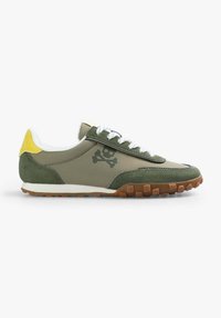 Des chaussures de sport vertes avec un dessus lisse, des accents en suède, des lacets blancs, une semelle en caoutchouc, et un graphique de skull et os croisés sur le côté.