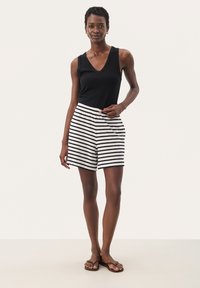 Top senza maniche nera abbinato a pantaloni corti a righe bianche e nere, con vita elastica e vestibilità comoda. Sandali piatti completano il look.