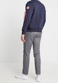 Felpa blu navy con collo rotondo e polsini a costine, decorata con una toppa della bandiera americana e un'etichetta rossa, abbinata a pantaloni grigi slim-fit.