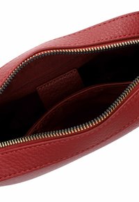 Červená kožená psaníčko s texturovaným povrchem, které má zlatý zip, vnitřní kapsu a měkkou tkaninovou podšívku.