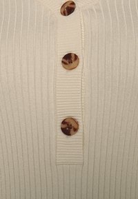 Gilet beige en maille côtelée avec quatre boutons marron marbrés, doté d'une patte de boutonnage et d'un motif texturé sur toute la surface.