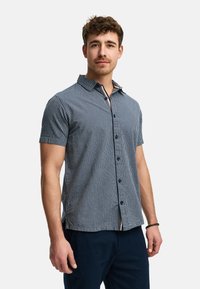 Camisa de hombre de manga corta en rayas verticales azules y blancas. Cuenta con un cierre frontal de botones, cuello y acentos en contraste cerca del escote.