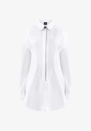 Valkoinen kauluspaita, jossa on pitkät hihat ja napit edessä. Sisältää muotoiltuja saumoja ja liehuvan helman, mikä luo rakenteellisen siluetin.