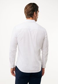 Camicetta bianca a maniche lunghe con colletto button-down, design aderente e dettaglio del giromanica sul retro. Materiale in cotone con texture liscia.