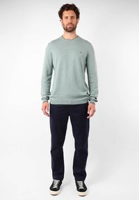 Pull en maille texturée vert clair à manches longues et col rond ; associé à un pantalon bleu marine foncé et des baskets noires avec des lacets blancs.