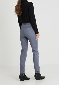 Grå skräddarsydda byxor i slät tyg, med en figurnära design och bakfickor, i kombination med en svart långärmad skjorta och klackstövlar.