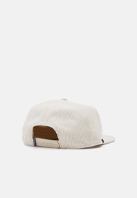 Beige kordbársony snapback sapka állítható műanyag pánttal és kis szövetcímkével a hátoldalon, fehér háttér előtt bemutatva.