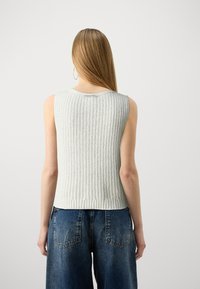 Light gray ribbed knit sleeveless top featuring a round neckline, textured fabric, and a fitted hem, paired with loose-fitting blue denim jeans.