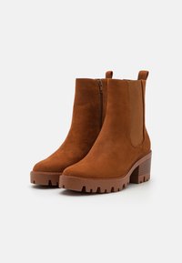 Bottines en suède marron avec fermetures éclair latérales, semelles en caoutchouc épaisses et talons carrés texturés. Dotées de panneaux latéraux élastiques pour un enfilage facile.