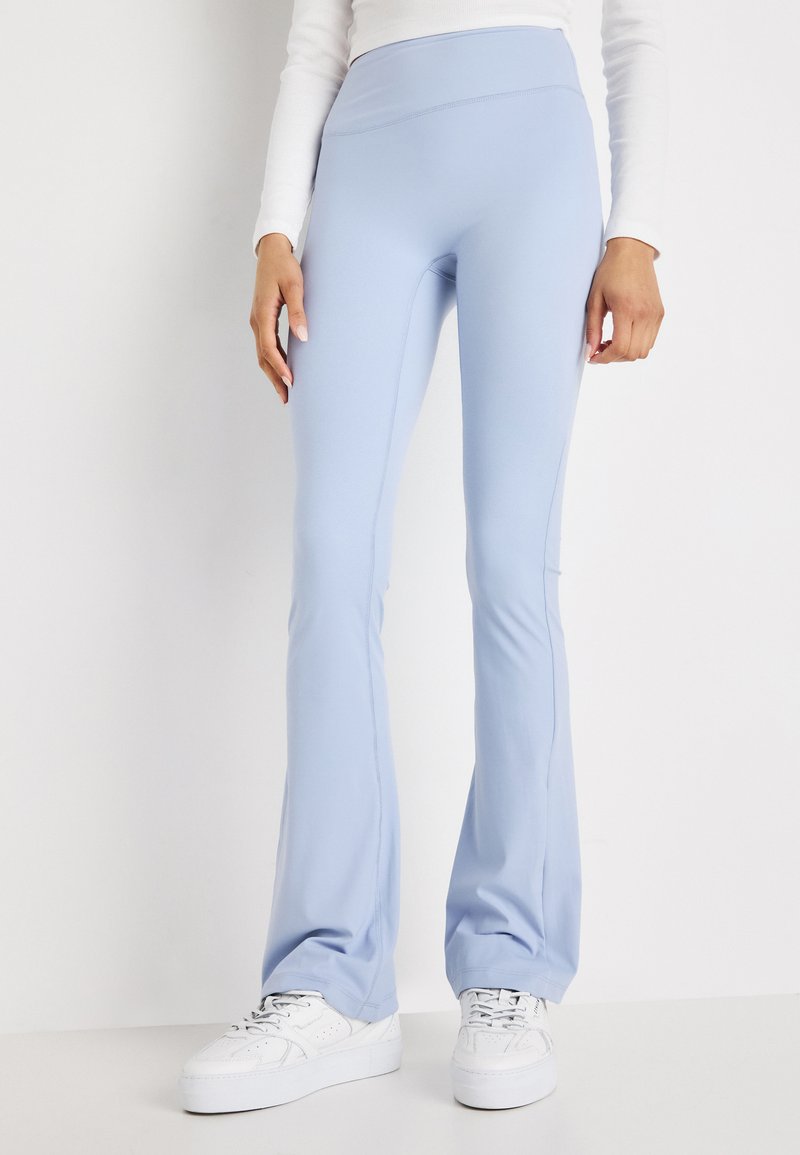 Leggings a campana di colore azzurro chiaro realizzati in tessuto elasticizzato, con vita alta e superficie liscia, abbinati a sneaker bianche.