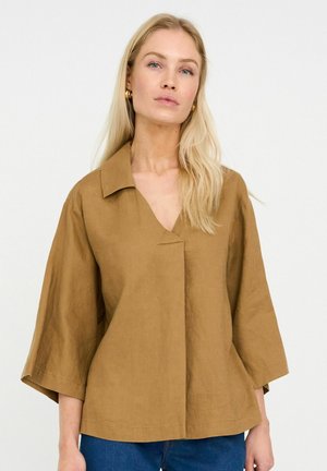 Barna len blúz V-nyakkivágással és nagy gallérral. Háromnegyedes ujjakkal és kényelmes szabással rendelkezik. Sima textúra, minimális díszítéssel.