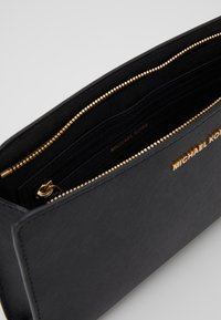 Svart läderhandväska med strukturerad yta, guldfärgad dragkedja och flera interna fack med tryckt varumärkeslogotyp inuti.