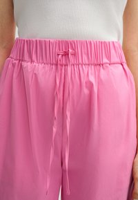 Roze elastische taillebroek met een trekkoord, gemaakt van soepele stof. Bevat gathered details voor een ontspannen, losse pasvorm.