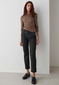 Zwarte slim-fit broek met twee verticale naden, gecombineerd met een aansluitend bruin shirt met lange mouwen. Model draagt zwarte instappers. Effen achtergrond.