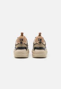 Zapatillas con un diseño negro y beige, parte superior de malla, suela gruesa y acentos texturizados. Logotipo "SM" en la parte trasera.