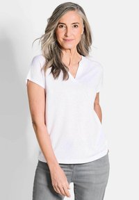 Witte korte mouwen V-hals shirt, zachte textuur, relaxte pasvorm, gecombineerd met lichtgrijze jeans. Eenvoudig ontwerp, geen zichtbare patronen of accenten.