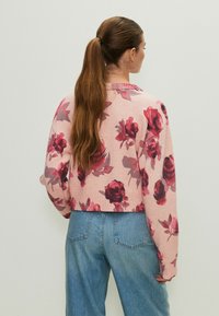 Felpa corta rosa con motivo floreale rosso e viola, con polsini e orlo a costine, abbinata a jeans in denim blu a vita alta.