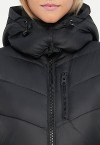 Veste doudoune noire avec un col haut et une capuche ajustable. Dotée d'une fermeture éclair et de coutures matelassées horizontales pour l'isolation.