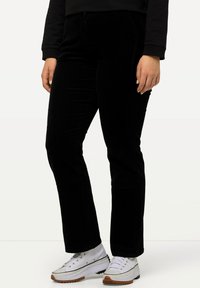 Zwarte corduroy broek met een rechte pasvorm, voorzien van voorzakken en een soepele textuur. Gepaard met witte sneakers en zwarte opgerolde mouwen.