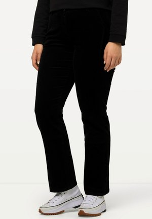 Pantaloni di velluto nero con una vestibilità dritta, dotati di tasche anteriori e una texture liscia. Abbinati a sneakers bianche e maniche nere risvoltate.