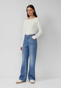 Weißes Langarmoberteil mit einem Bootsausschnitt, kombiniert mit hochgeschnittenen, hellblauen weiten Jeans und Sneakers. Schlichtes, lockeres Design.