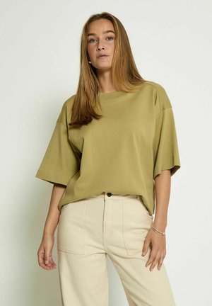 Olijfgroen oversized katoenen t-shirt met korte mouwen en een ronde hals, gecombineerd met lichtbeige hoge taille broeken.