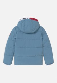 Modrá zateplená zimní bunda s kapucí, dlouhými rukávy a žebrovanými manžetami, se znakem Tommy Hilfiger v červené, bílé a modré barvě na okraji kapuce a rukávu.