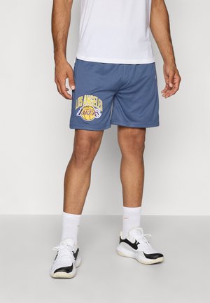 Blå mesh shorts har et fremtrædende gult "Los Angeles Lakers" print og et basketball grafik. Båret med hvide sneakers og sokker.