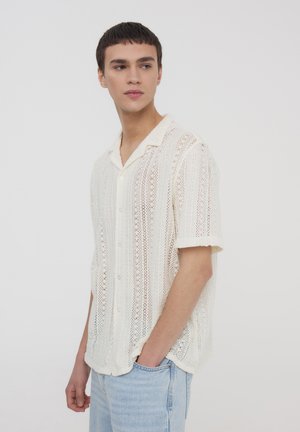 Camicia a maniche corte con bottoni in un motivo a maglia avorio, caratterizzata da una vestibilità rilassata, una trama leggera e un delicato design a trama aperta.