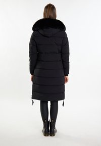 Sort polstret frakke med falsk pelskrave, knælang, med vandret quiltning, justerbare snore og parret med sorte leggings og støvler.