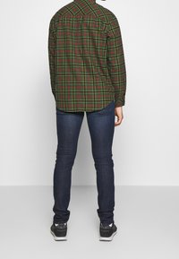 Grön och röd rutig skjorta med långa ärmar, rund nederkant och knappmanchetter, ihop med mörkblå skinny jeans och svarta sneakers.