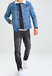 Denim jacket in light blue with a cream faux fur collar, worn over a dark grey shirt and black jeans, complemented by white sneakers.