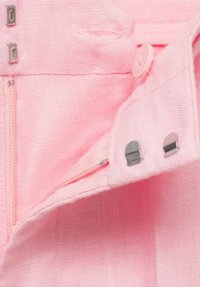 Light pink fabric with a textured finish; features a zipper pocket and metallic hardware accents, including buttons and clasps.