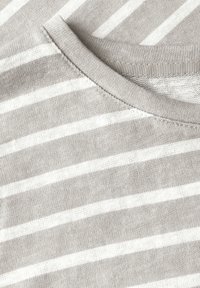 Ljusgrå bomullströja med vita horisontella ränder. Har en rund halsringning och synlig sömnad längs kragen. Mjuk textur.